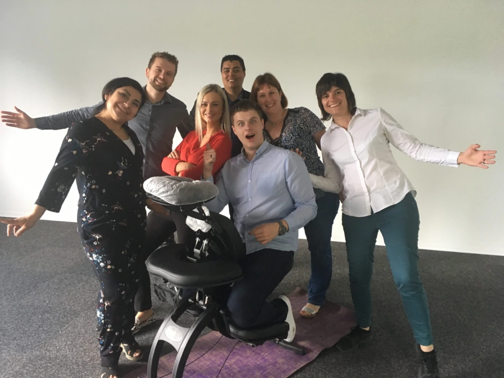 Groupe de collaborateurs autour d’une chaise de massage lors d’un atelier bien-être en entreprise